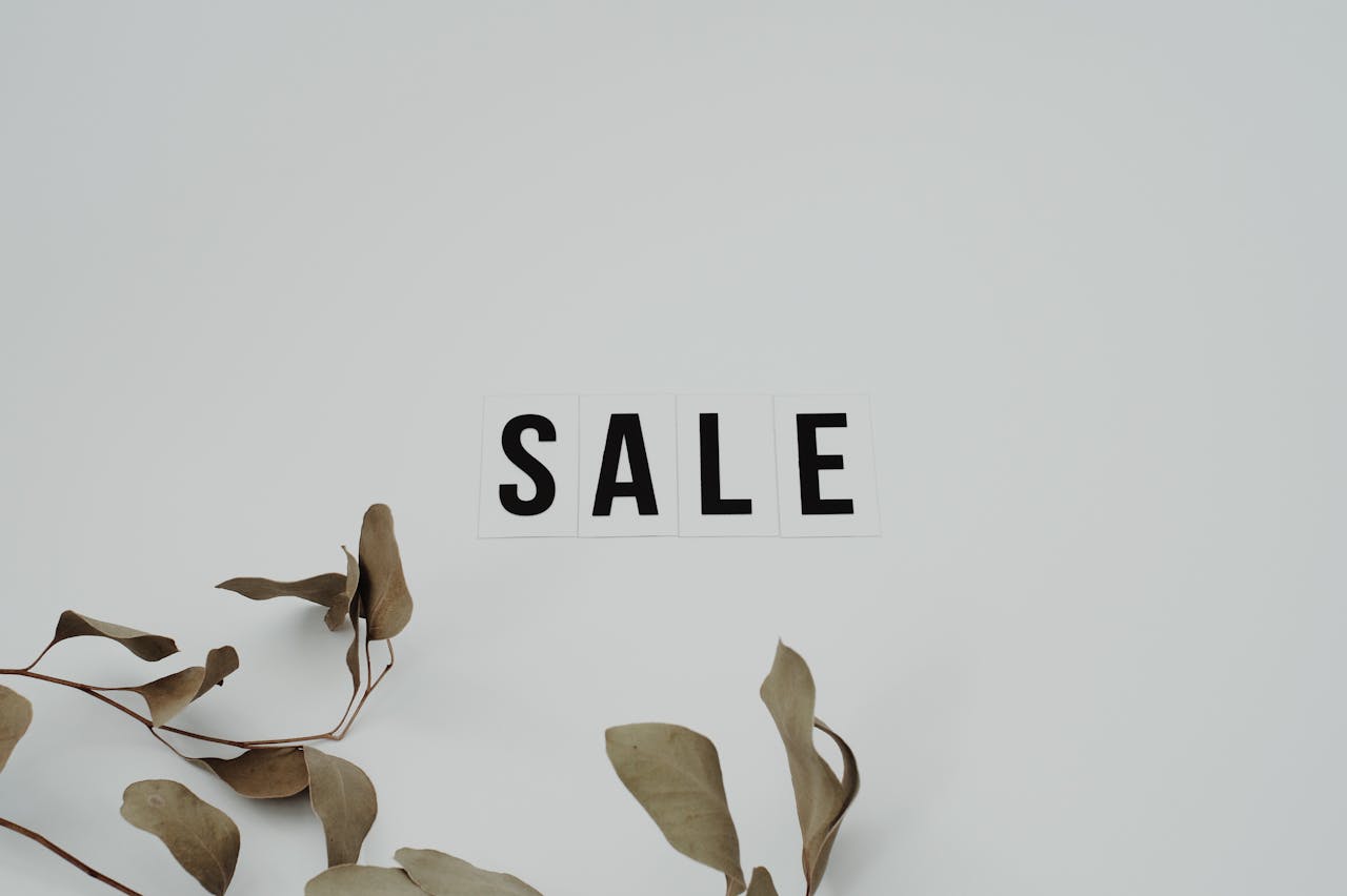 Minimalist SALE sign with eucalyptus leaves on white background, perfect for retail marketing.